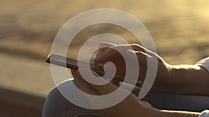 Close-up young business woman using smartphone at sunset, female hands typing smartphone keyboard