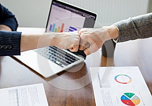 Close up of young businessman and businesswoman making a fist bump on building background. Business people wear suit do