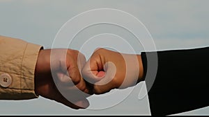 Close-up of young businessman and businesswoman making fist bump on sky background. Business success and teamwork concept.