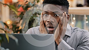 Close-up young businessman looking at laptop screen getting bad news surprised shocked man holding head found error