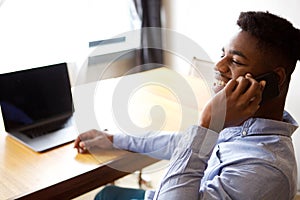Close up young businessman talking on phone while sitting at desk with laptop computer