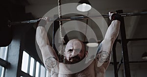 Close-up young Caucasian athlete man lifting heavy barbell in large hardcore gym hall. Ambition and challenge concept.