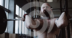 Close-up young Caucasian athlete man lifting heavy barbell in large hardcore gym hall. Ambition and challenge concept.