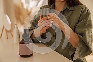 Close-up of young caucasian girl applying moisturizer on her hands while sitting at table.