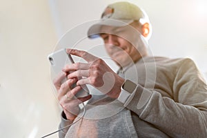 Close up young caucasian man in baseball cap looking and using mobile smart phone at home. Facetime video calling with
