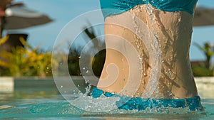 CLOSE UP: Young Caucasian woman in bikini jumps out of stunning tropical pool.