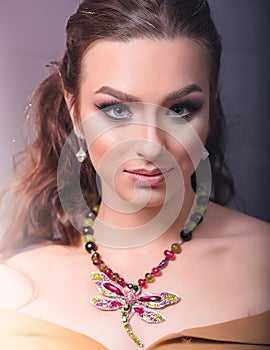 Close-up of Young Caucasian Woman with Golden Jewelry. She Wears a Statement Necklace With a Dragonfly and Colorful Stones, a Pair