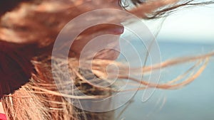 Close-up of a young Caucasian woman's hair fluttering in slow motion in the wind. Shallow depth of field. Girl in red