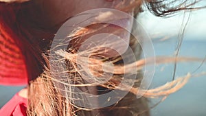 Close-up of a young Caucasian woman's hair fluttering in slow motion in the wind. Shallow depth of field. Girl in red
