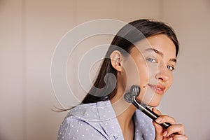 Close- up young caucasian woman using her face massager in morning.