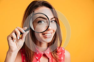Close up of young cheerful brunette woman looking through magnifying glass