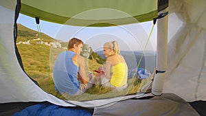 CLOSE UP: Young couple sitting in front of their tent and texting their friends.