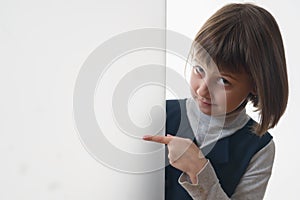 Close up young cute girl looking outside behind white empty banner. She pointing to white wall. Free copy space area