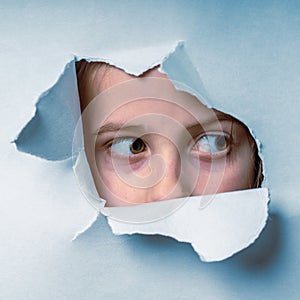 Close up young cute scared child girl  looking through a hole in the paper wall