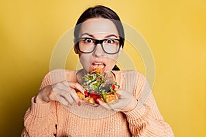 Close-up young emotional girl eating Italian pizza isolated on yellow studio background. World pizza day