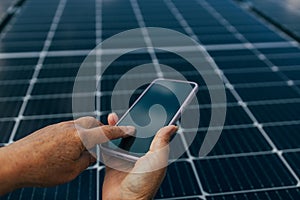 Close-up of young engineer hand holding smartphone on panel background on sunny day, green alternative energy concept