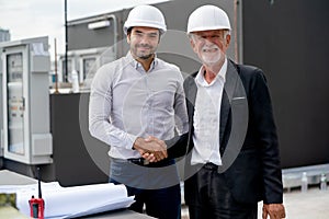Close up young engineer shake hands with senior coworker and stay in front of line of air vent in construction site to express
