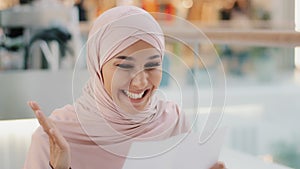 Close-up young excited happy arab woman in hijab receiving letter reading good incredible news smiling excellent medical