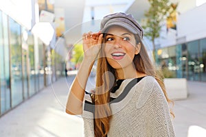 Close up of young fashion woman holding baker boy hat in shopping mall. Young pretty trendy girl posing in street with fashion