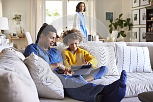 Close up of young father sitting on sofa in the living room with his pre-teen daughter using tablet computer, selective focus, mum
