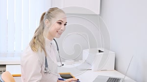 Close-up. A young female doctor in a white coat is talking to a patient and completing a survey sheet.