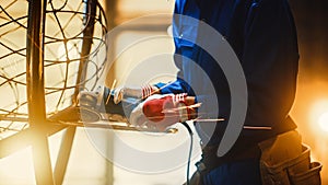 Close Up of Young Female Fabricator in Blue Jumpsuit. She is Grinding a Metal Tube Sculpture with