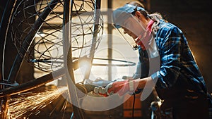 Close Up of Young Female Fabricator in Safety Mask. She is Grinding a Metal Tube Sculpture with an