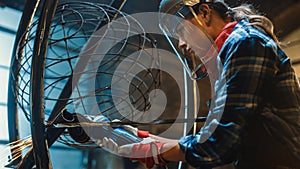 Close Up of Young Female Fabricator in Safety Mask. She is Grinding a Metal Tube Sculpture with an