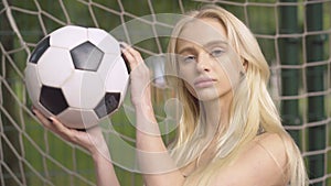 Close-up of young female goalkeeper posing with ball on outdoor playground. Portrait of confident beautiful Caucasian