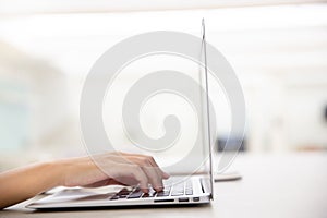 Close up of young female hands using laptop in modern office or loft near by the window