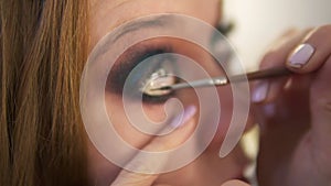 Close up of young female model is being maked up in studio. Artist is applying black liner to lower lid of the right eye