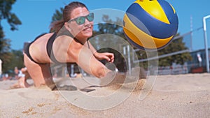 CLOSE UP: Young female volleyball player dives into the sand to save a point.