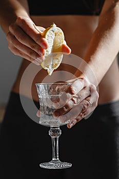 Close up of young fit slim woman preparing water with lemon juice. Morning ritual. Healthy antioxidant. Slimming diet