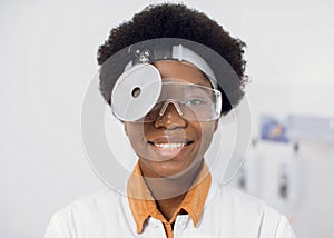 Close up of young friendly smiling African American woman doctor ent otolaryngologist, wearing hed frontal reflector and