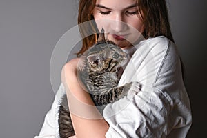 Close up of young girl holding a baby cat on gray background. Female hugging her kitty. Adorable domestic pet concept.