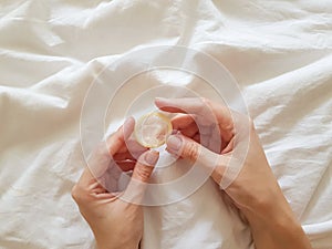 Close up. A young girl holds a condom in a hand in a white bed. The concept of sex and eroticism. photo
