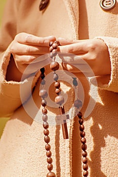 Close up young girl praying and holding a wooden rosary. Vertical image