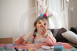 Close-up of a young girl showcasing a plastic animal figure, with a soft-focused background featuring art supplies and