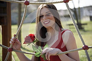 Close-up of young girl smiling with red rose in a public park.