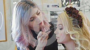 Young makeup artist applying cosmetics on model`s eyes.