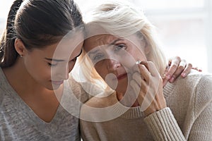 Close up young grown up worried daughter hugging frustrated mother.