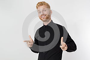 Close up of young guy with redhead and red beard isolated on white background. Stylish man in black shirt pointing copy space.