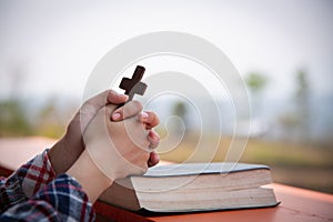 Close up young hands holding wooden cross over holy bible and praying. christian concept