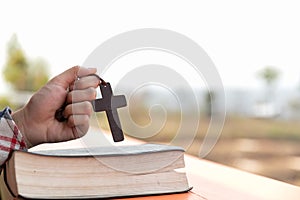 Close up young hands holding wooden cross over holy bible and praying. christian concept