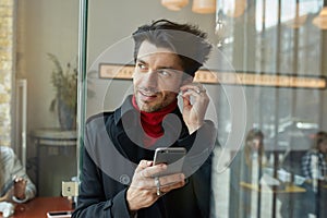 Close-up of young handsome dark haired unshaved male inserting earpiece while listening to music and looking positively aside,