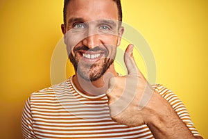 Close up of young handsome man wearing casual t-shirt over yellow isolated background doing happy thumbs up gesture with hand