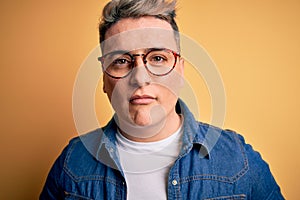 Close up of young handsome modern man wearing glasses and denim jacket over yellow background with a confident expression on smart