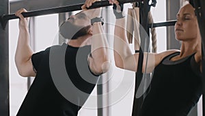 Close-up young happy fit Caucasian man and woman doing chin-ups together. Exercising with personal fitness coach.