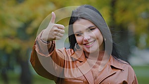 Close-up young happy hispanic woman standing outdoors smiling white healthy toothy smile looks at camera showing thumbs