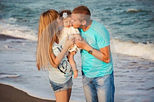 Close up of young happy loving family hugging and kissing small daughter at beach together near the ocean, happy